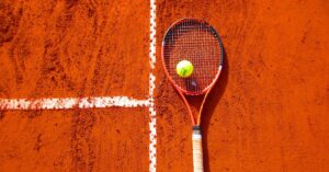 Tennis racket and ball on red clay court, ideal for sports-themed content.